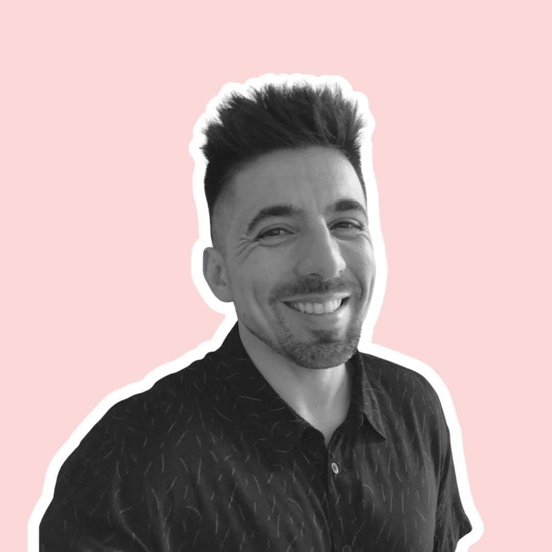 Andres Saldias with a short, textured hairstyle and facial hair, set against a soft pink background.