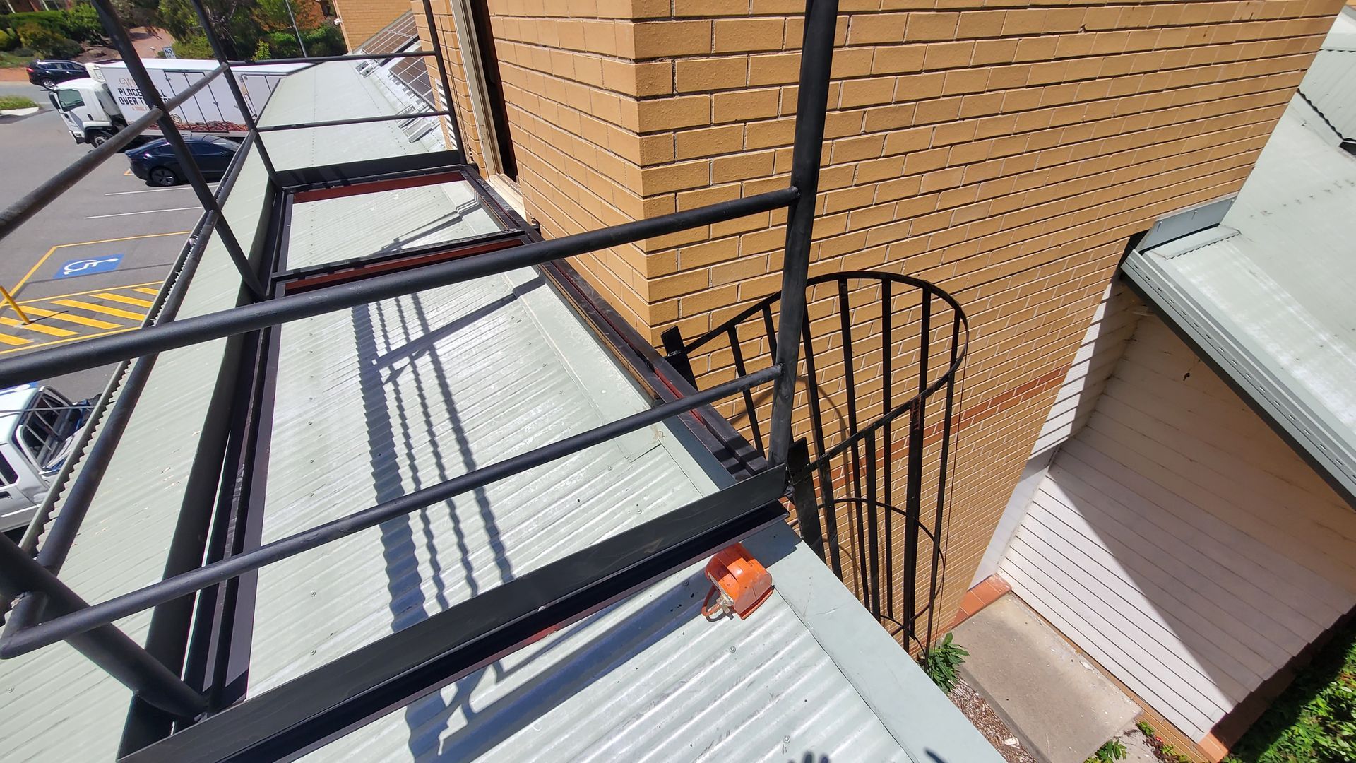 Balcony view with black railing, brick wall, and metal stairwell beside a building.