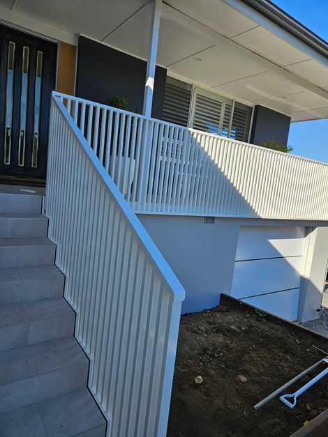 Concrete outdoor ramp with white railings leading up to a building entrance next to stairs.