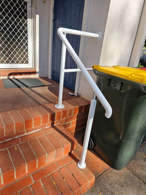 White handrail beside brick front steps next to a green wheelie bin and a blue door