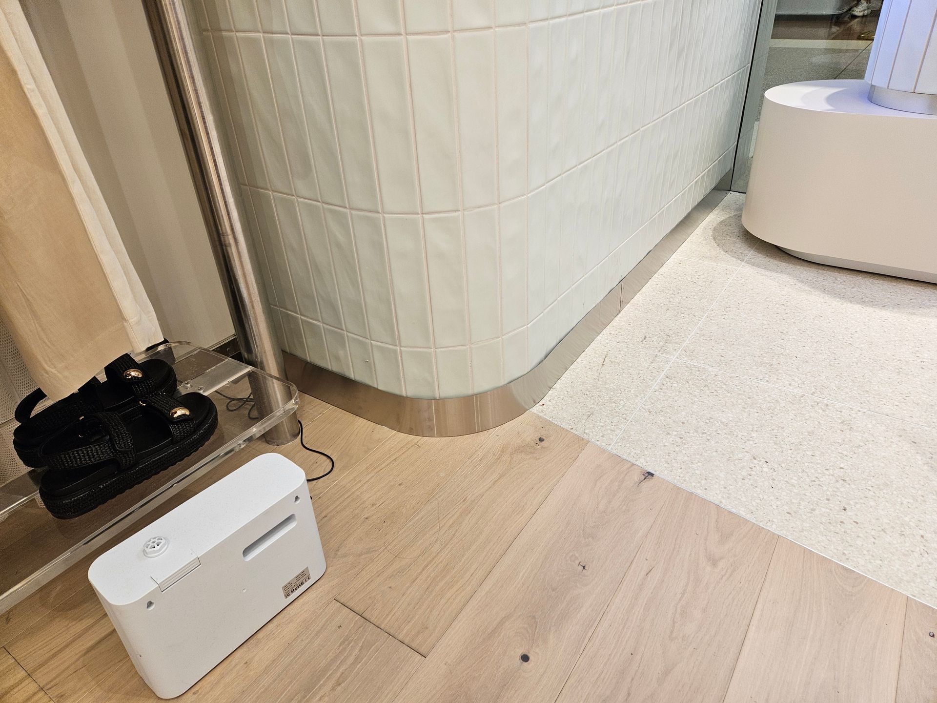 White robot vacuum in a bright room beside shoes and a wooden shelf