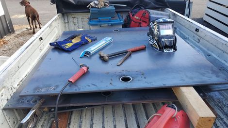 Tools on a blue workbench in a truck bed, with hammers, pliers, a drill, and a black case.