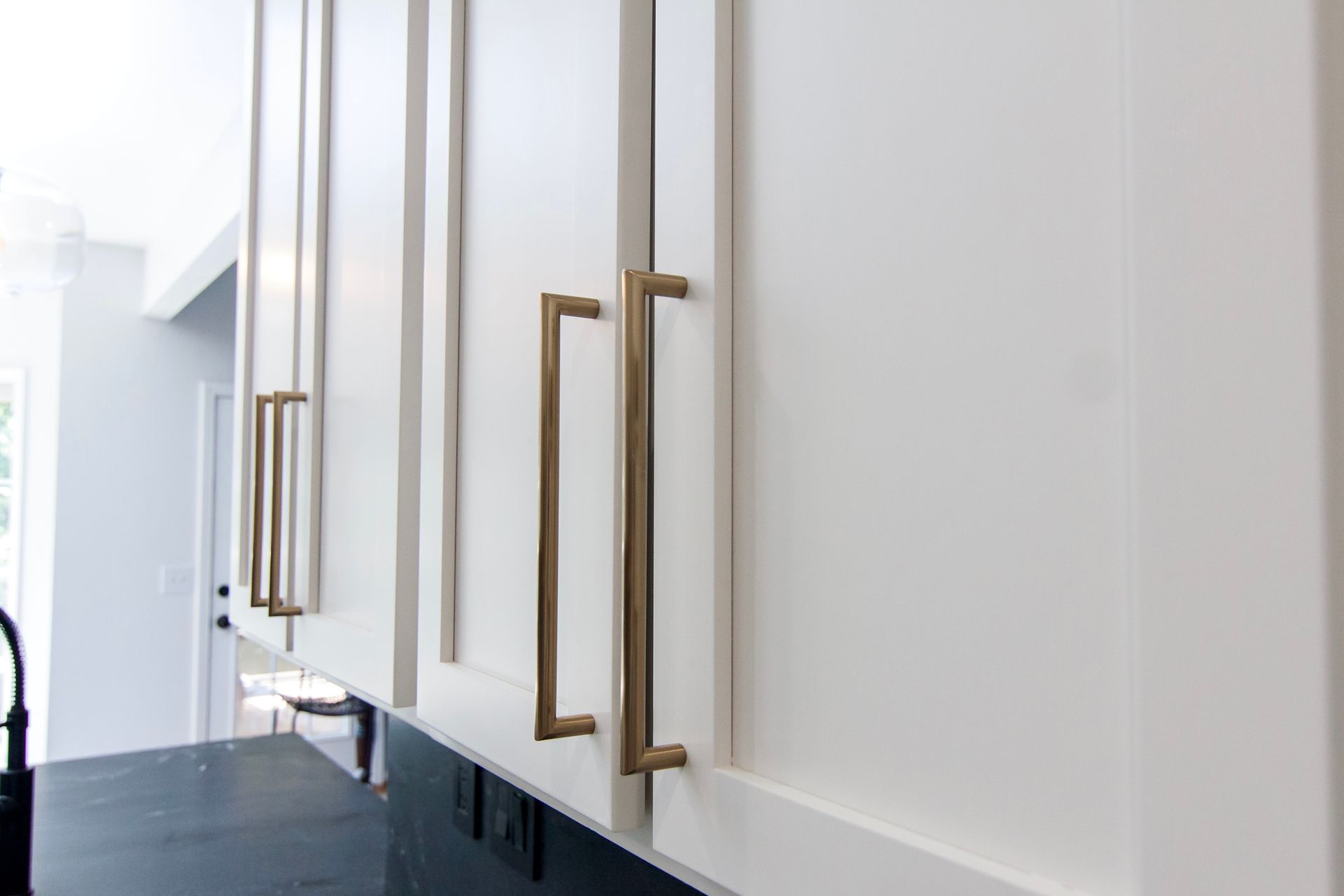 Row of white kitchen cabinets with long brass handles in a bright modern interior
