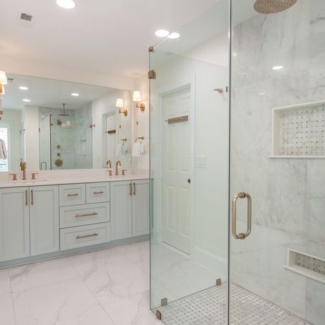 Bright marble bathroom with double vanity, large mirror, and glass shower enclosure.