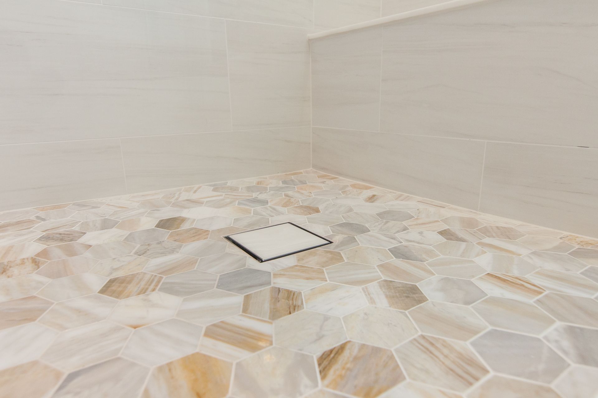 Tiled shower floor with a square drain in the center, beige and white stone pattern