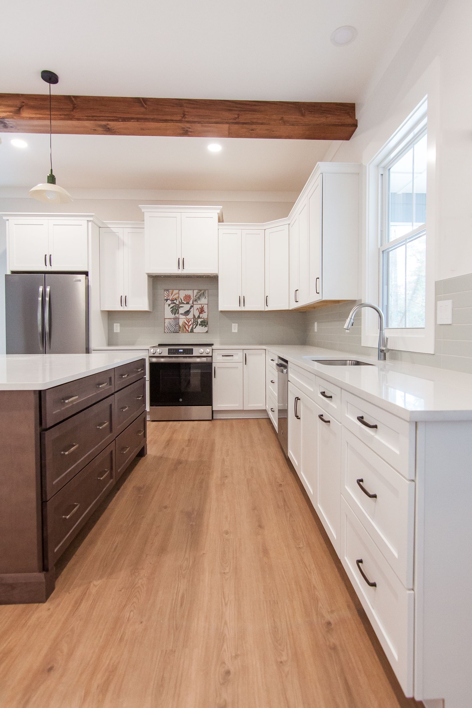 Bright modern kitchen with white cabinets, wood floors, stainless fridge, and dark island.