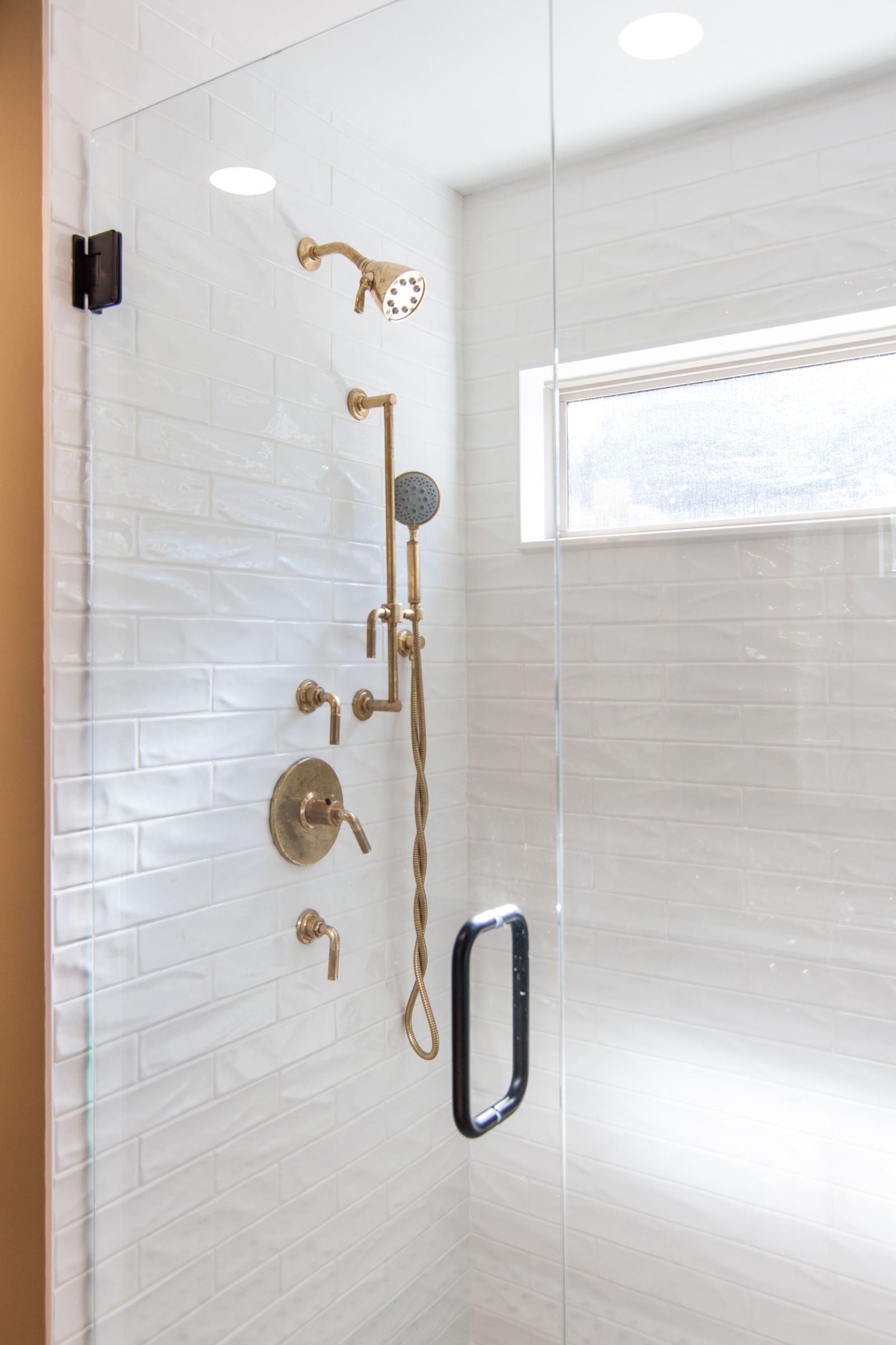 Gold shower fixtures in a white tiled glass shower enclosure