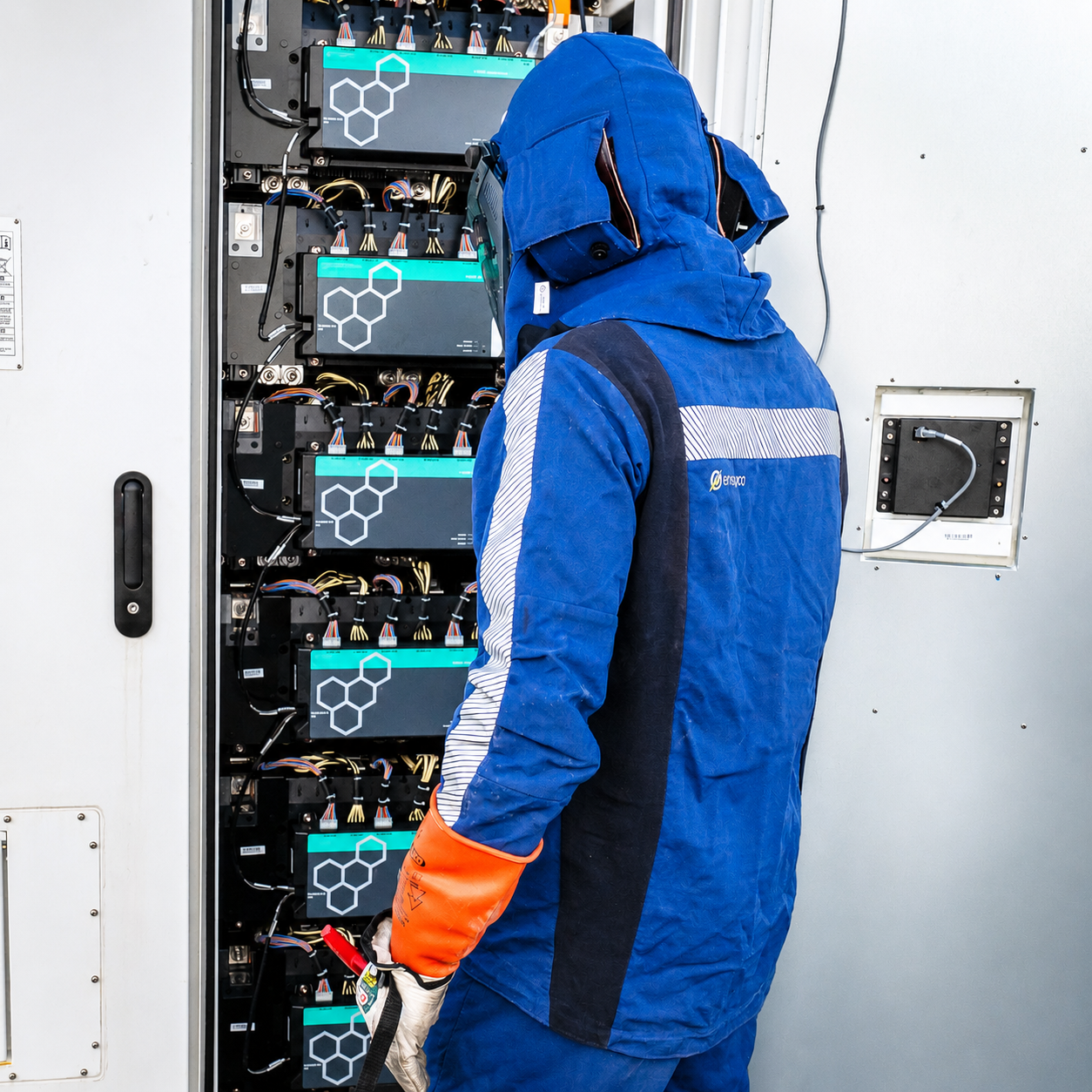 Technician in blue safety gear inspecting electrical equipment in a control cabinet