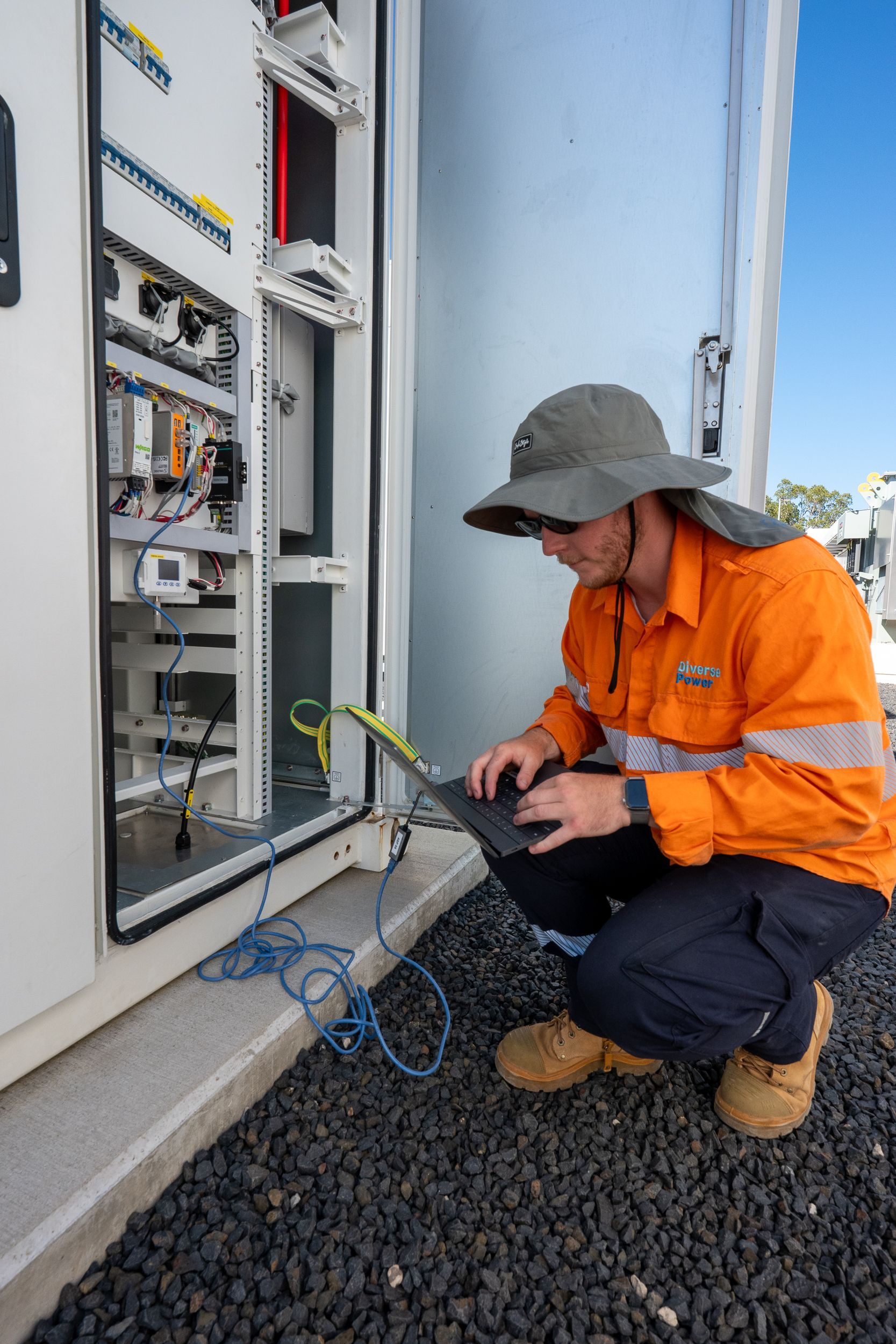 Technician in orange safety gear inspecting an open electrical control cabinet outdoors
