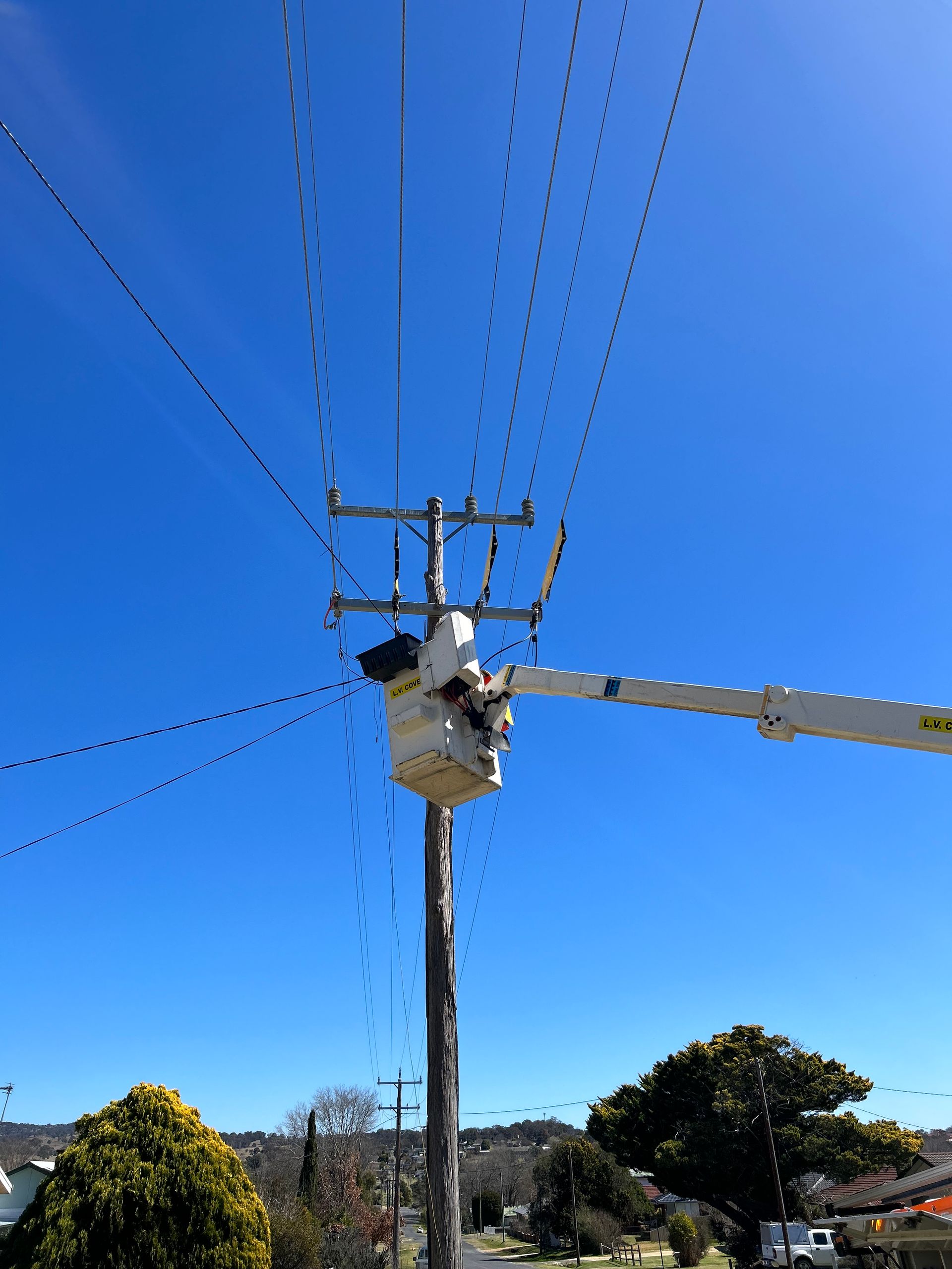 Utility worker in a bucket lift repairing power lines against a clear blue sky