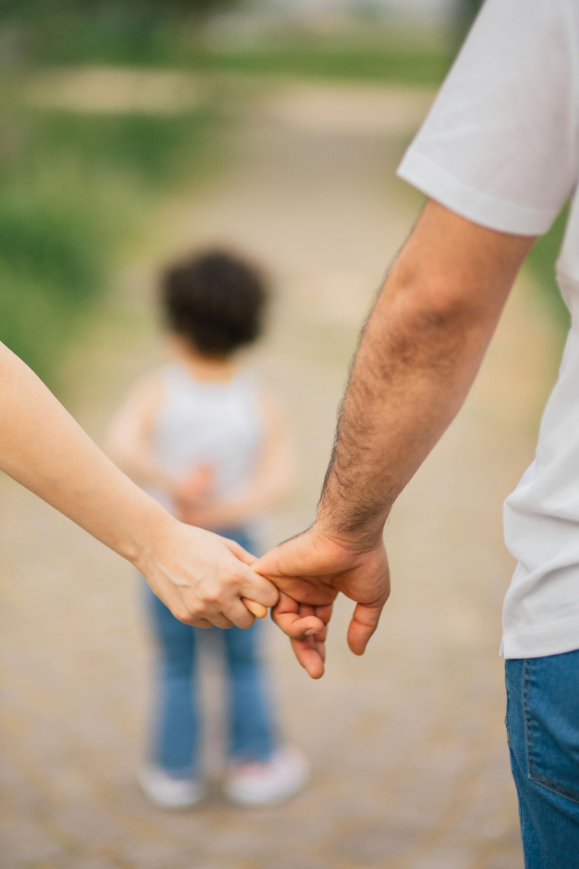 Two adults holding hands with a child blurred in the background on a walkway