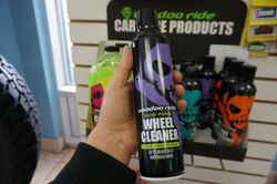 Une main tient une bouteille noire et violette de nettoyant pour roues Voodoo Ride dans un magasin.