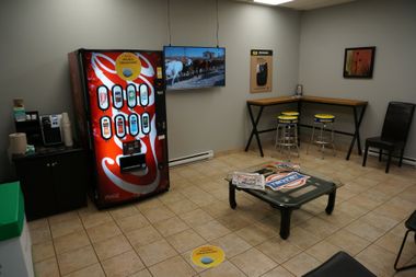 Une salle d'attente avec machine à soda, TV, table, chaises et machine à café.