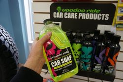 Une personne tenant une bouteille de savon pour voiture Voodoo Ride dans un magasin, entourée d'autres produits d'entretien automobile.