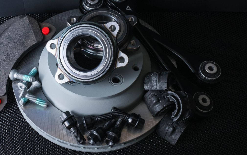 componenti delle sospensioni per auto, tra cui un disco freno, un cuscinetto ruota, un braccio oscillante e bulloni di fissaggio, su sfondo scuro.