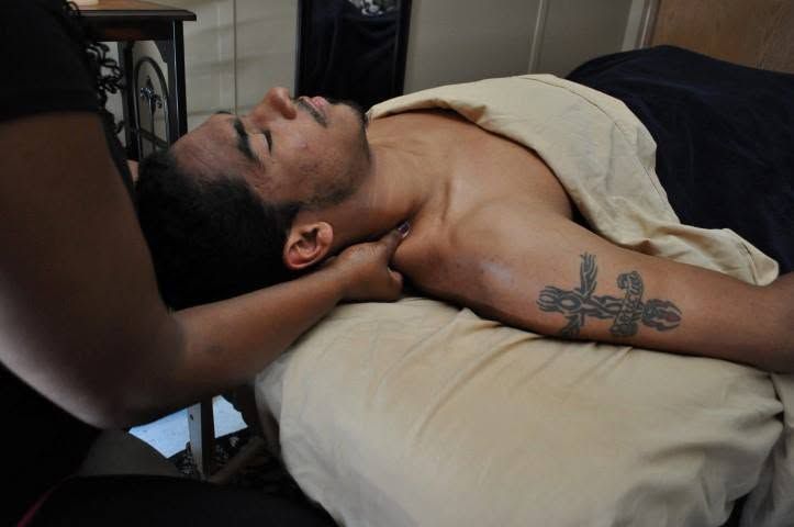 Person receiving a neck massage on a treatment table, eyes closed, with a tattoo visible on the arm.