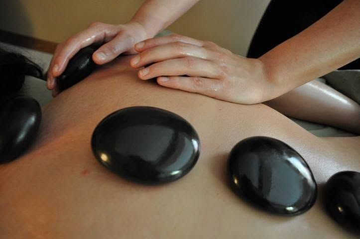 Hands massaging a back with smooth black hot stones on warm skin