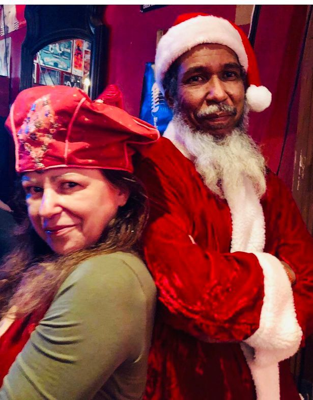 A man dressed as santa claus stands next to a woman wearing a red hat