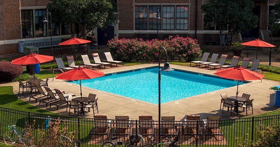 Pool surrounded by lounge chairs, tables with umbrellas on a sunny day.