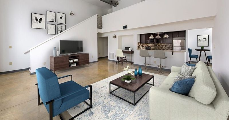 Loft apartment living room with stairs, a kitchen, and a blue armchair and couch.