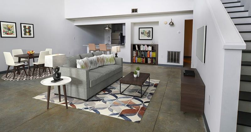 Modern living room with gray sofa, open kitchen, and staircase.