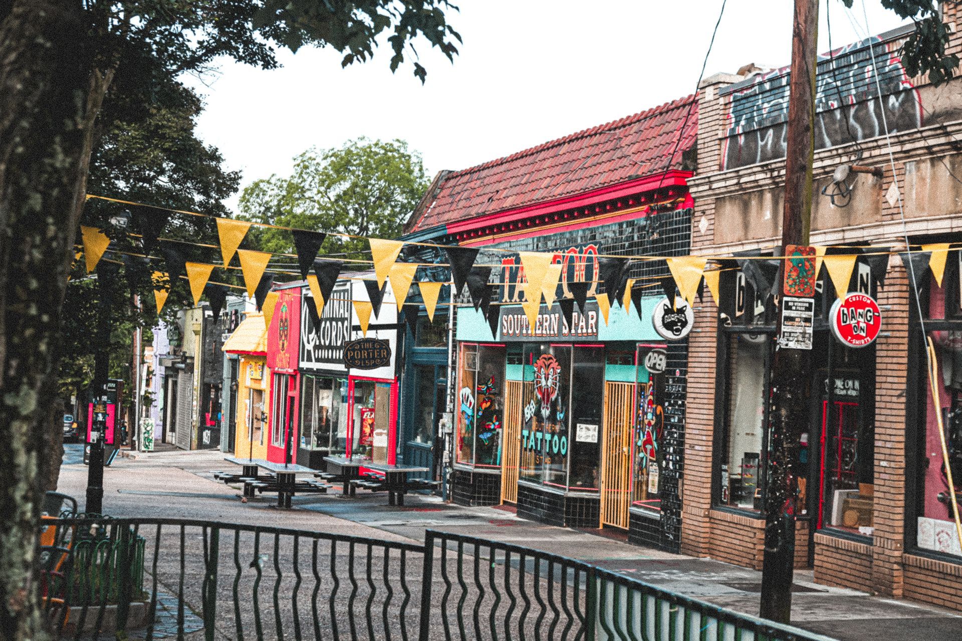 Street lined with colorful shops, decorated with bunting, a brick sidewalk and wrought iron fence.