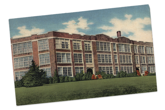 Brick school building with many windows, green lawn, blue sky with clouds.