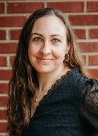A woman in a black shirt is smiling in front of a brick wall.