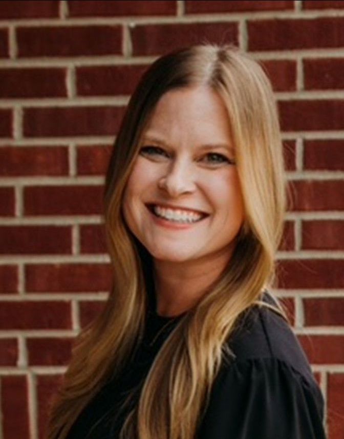 A woman is smiling in front of a brick wall.