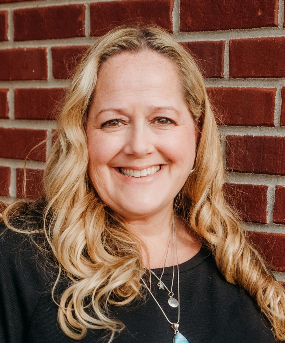A woman is smiling in front of a brick wall.