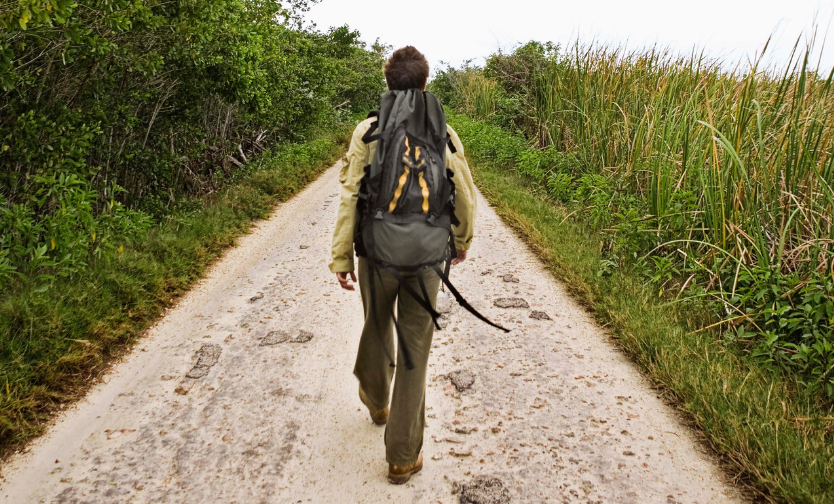 A person with a backpack is walking down a dirt road.