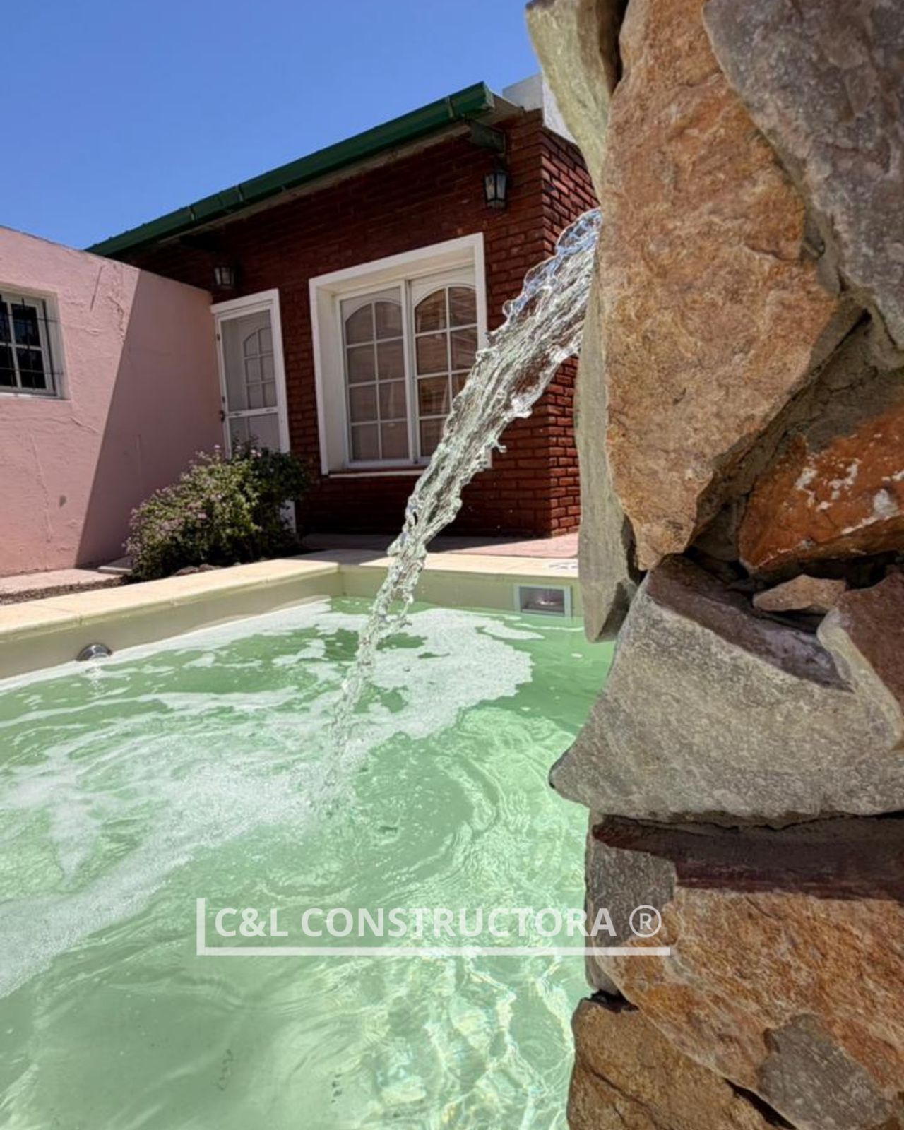 Agua cayendo en cascada en una pequeña piscina, al lado de un edificio de ladrillos.