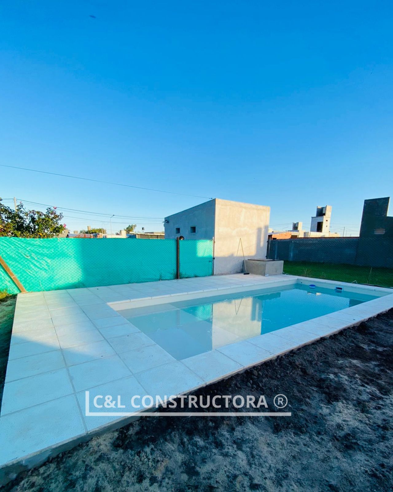 Piscina con azulejos blancos y pared turquesa, cielo azul nublado.