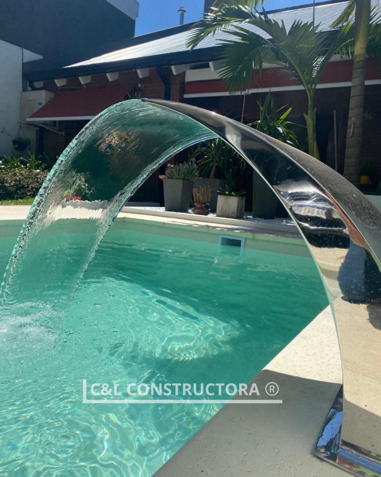 Piscina con fuente de agua arqueada, agua clara y entorno soleado.
