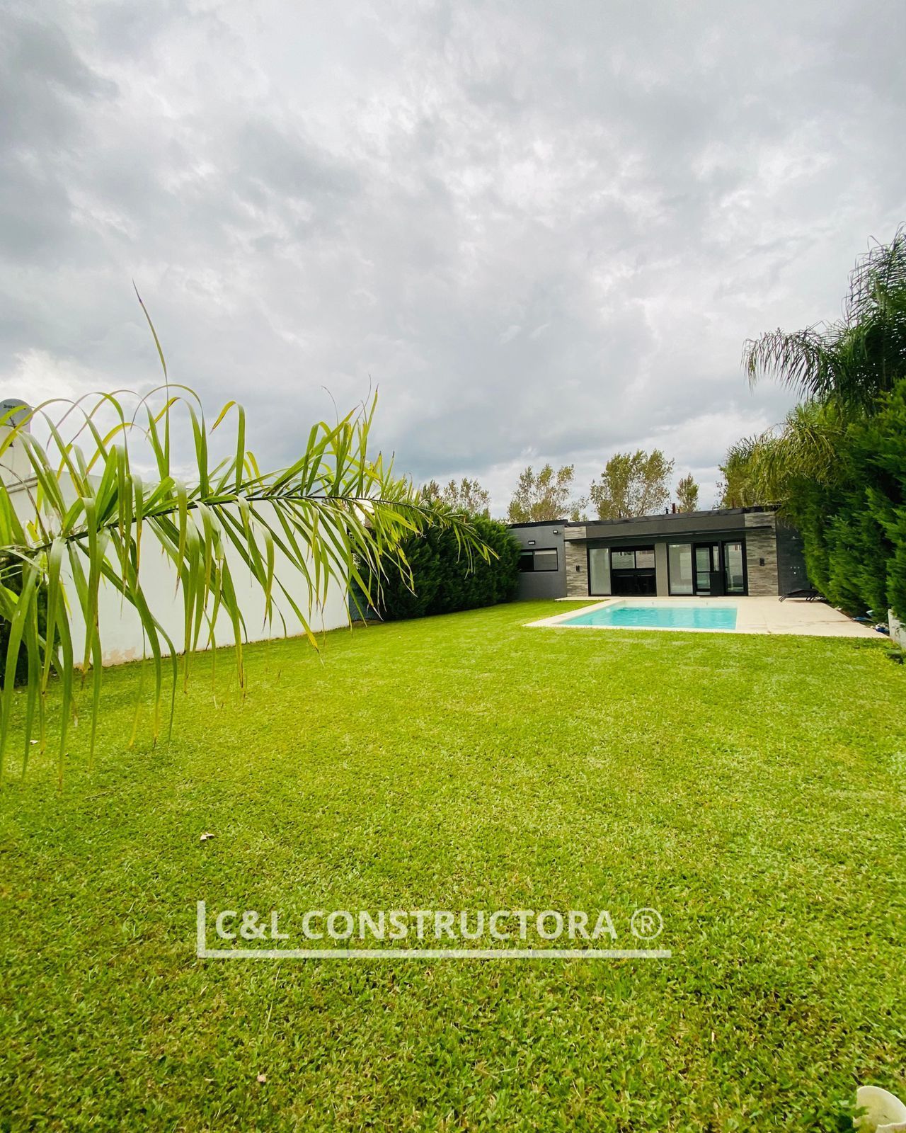 Césped con piscina y casa bajo un cielo nublado.