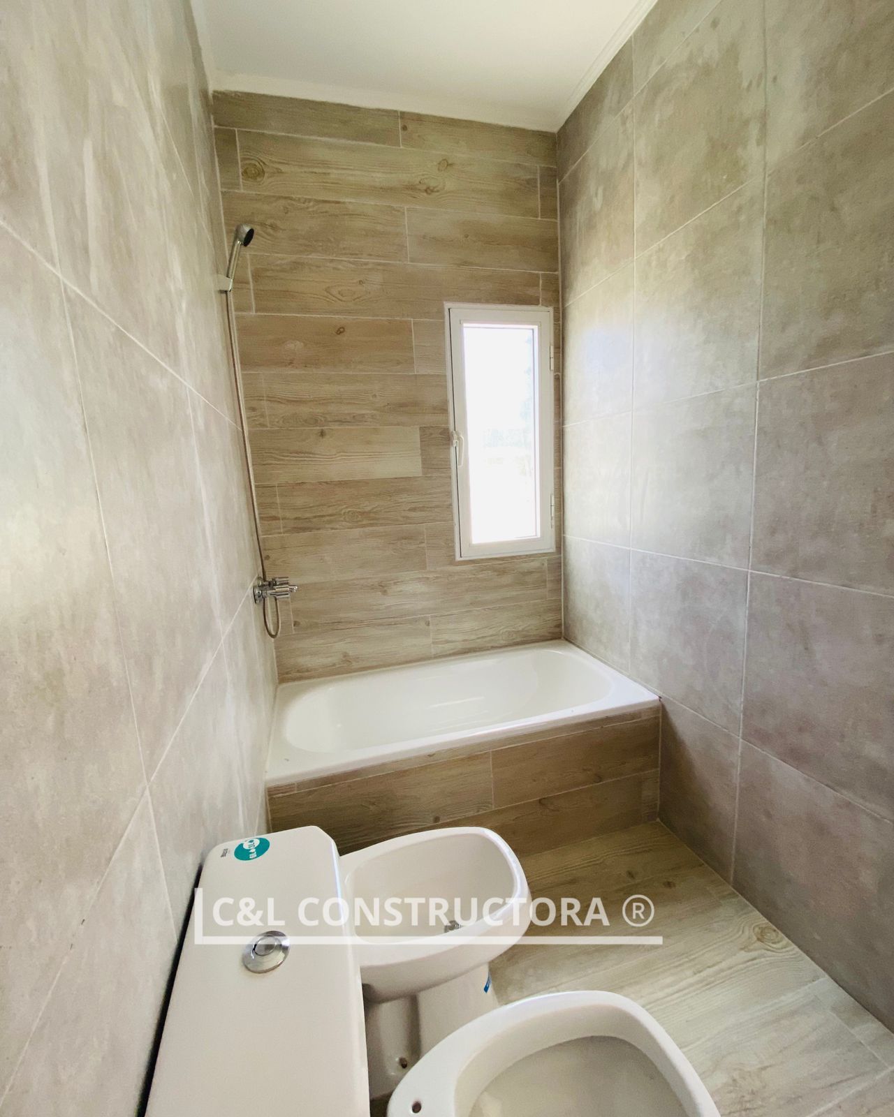 Baño con paredes alicatadas, bañera, inodoro, bidet y pequeña ventana.