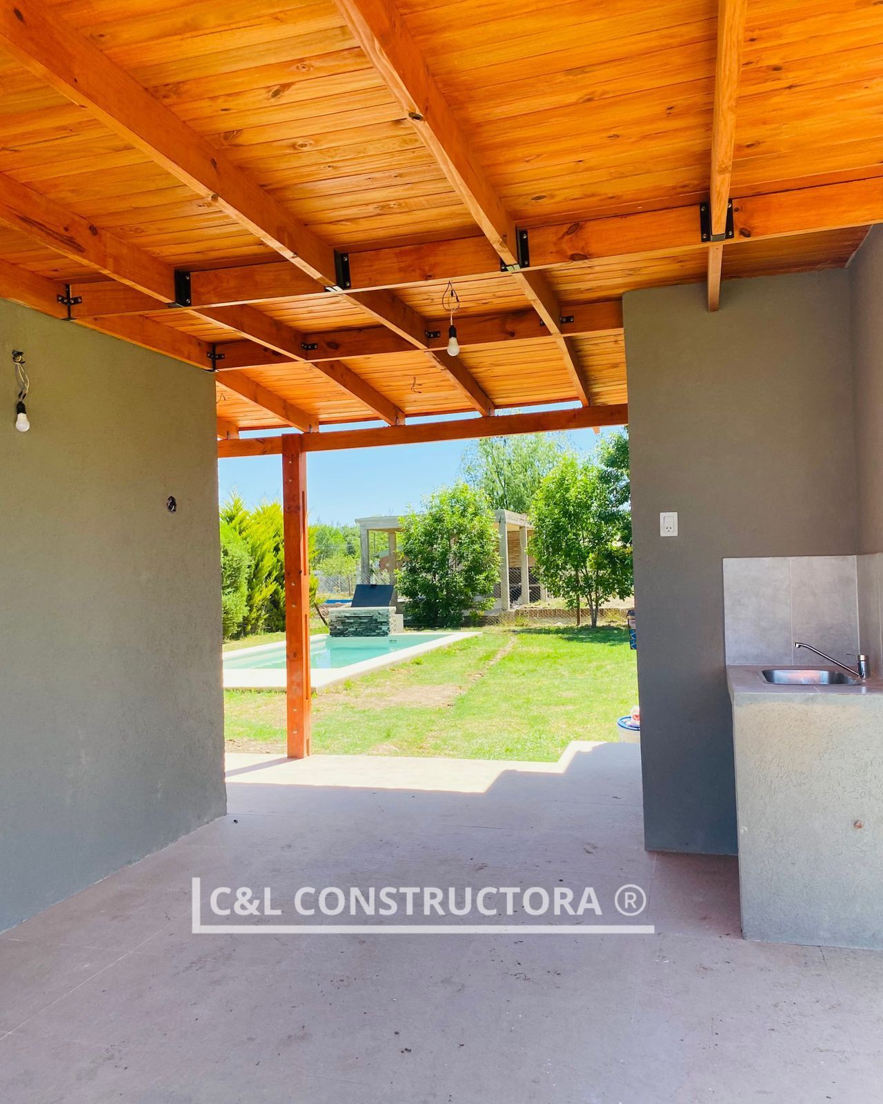 Patio al aire libre con techo de madera con vistas a la piscina y al jardín, con paredes grises y fregadero.
