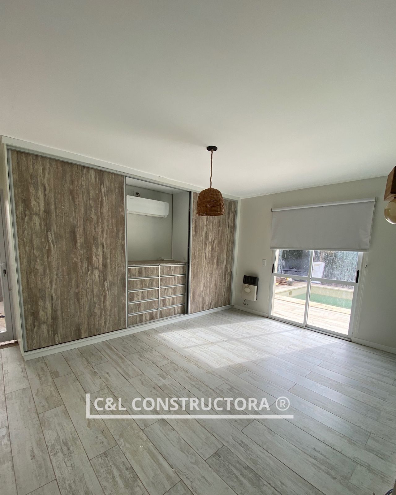 Dormitorio moderno con puertas corredizas de madera, pisos de colores claros, ventana con persianas y lámpara colgante.