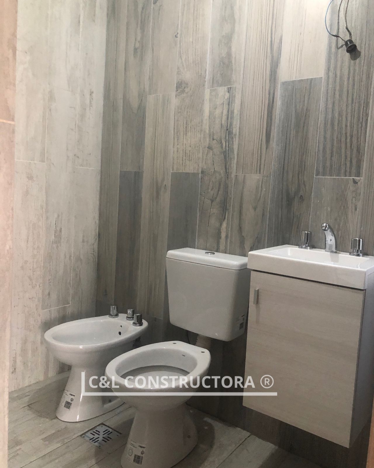 Baño con azulejos imitación madera gris claro. Bidé, inodoro y lavabo.