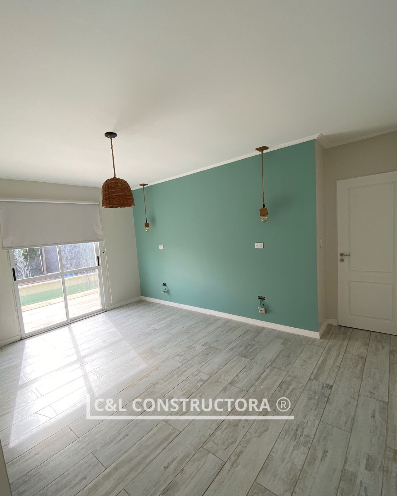 Habitación vacía con pared de acento verde claro, piso con apariencia de madera y dos luces colgantes.