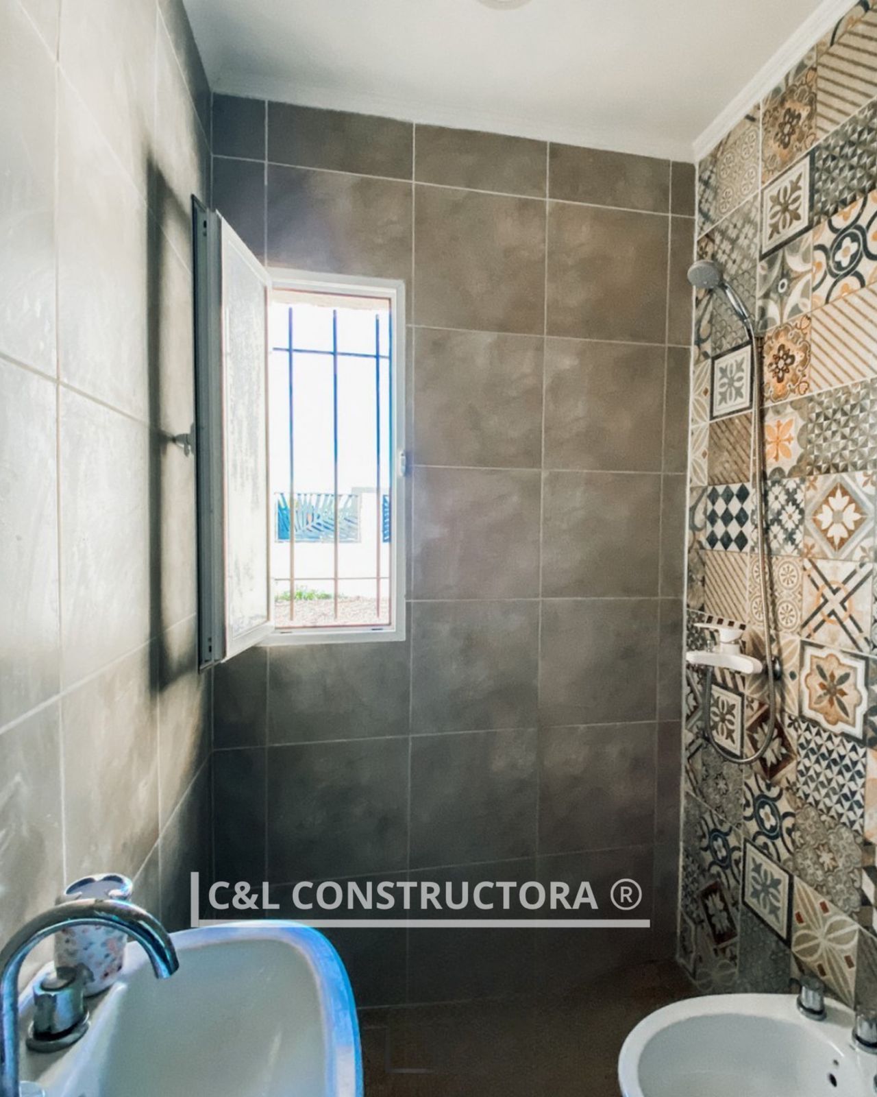 Baño con paredes alicatadas y ventana con persianas abiertas. Lavabo en primer plano, bidé 