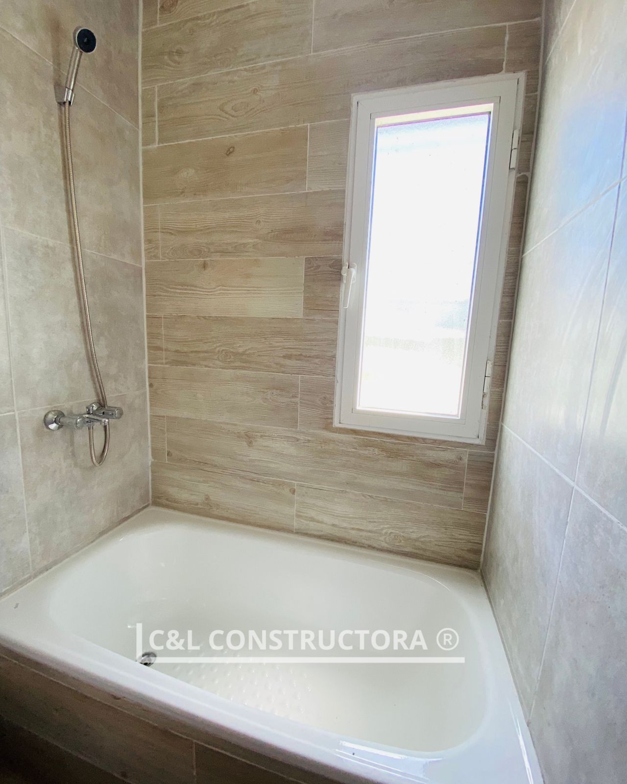 Baño con bañera blanca, paredes de azulejos beige y una pequeña ventana.