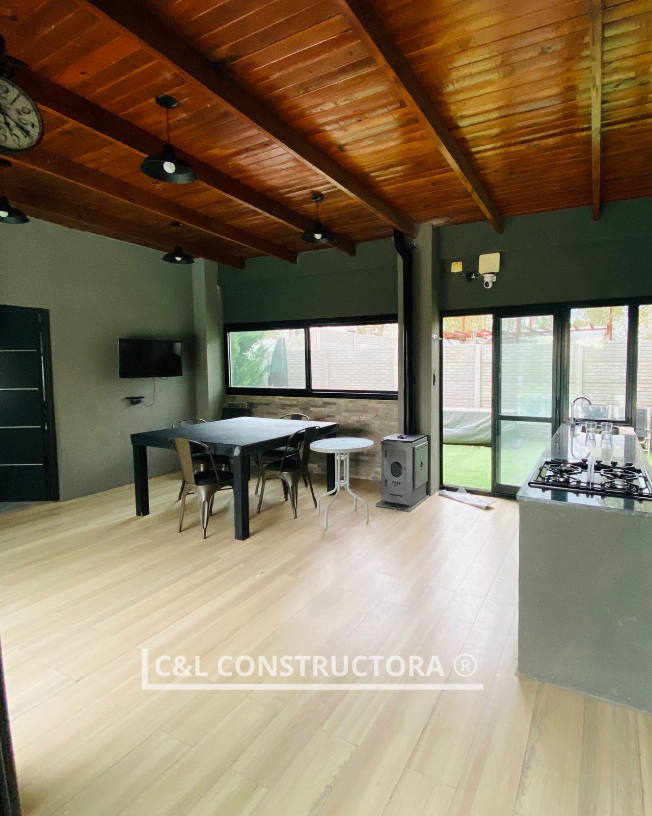 Cocina-comedor de concepto abierto con techo de madera, paredes oscuras y suelos claros. Cuenta con mesa, sillas y estufa.