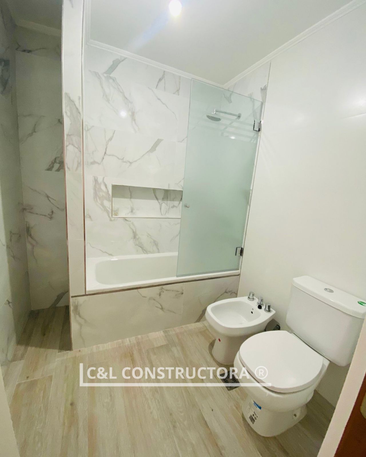 Un baño moderno con azulejos con estampado de mármol, bañera, ducha, inodoro y bidé.