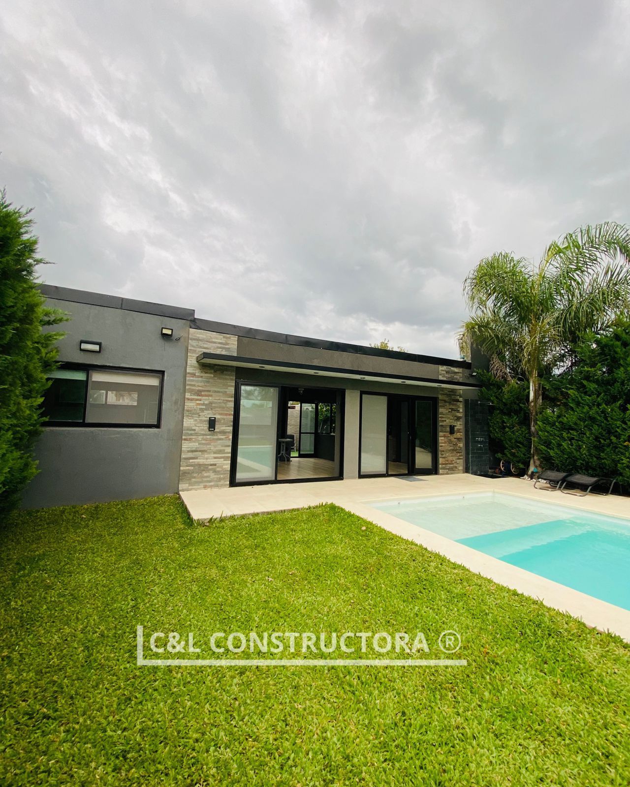 Casa moderna con piscina y césped bajo cielo nublado.