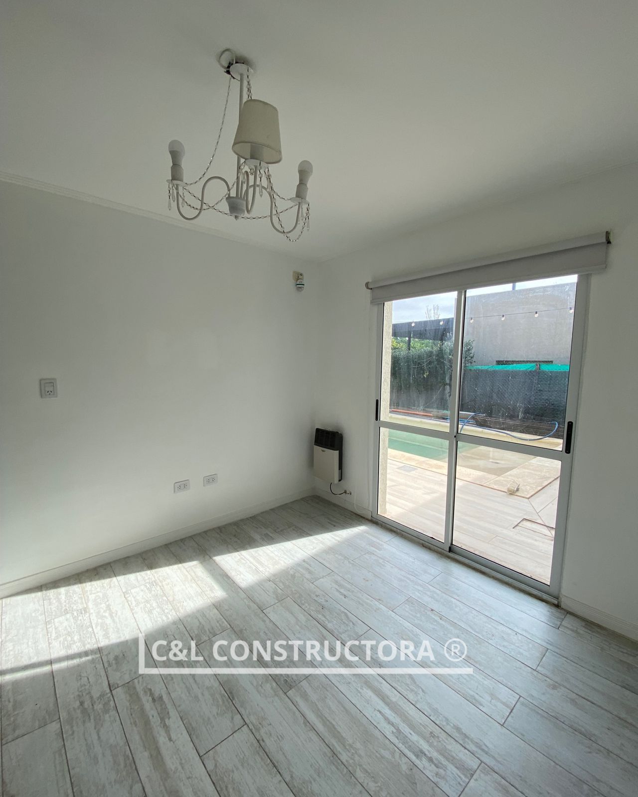 Habitación vacía con paredes blancas, puerta corrediza de vidrio, lámpara de araña y calentador.