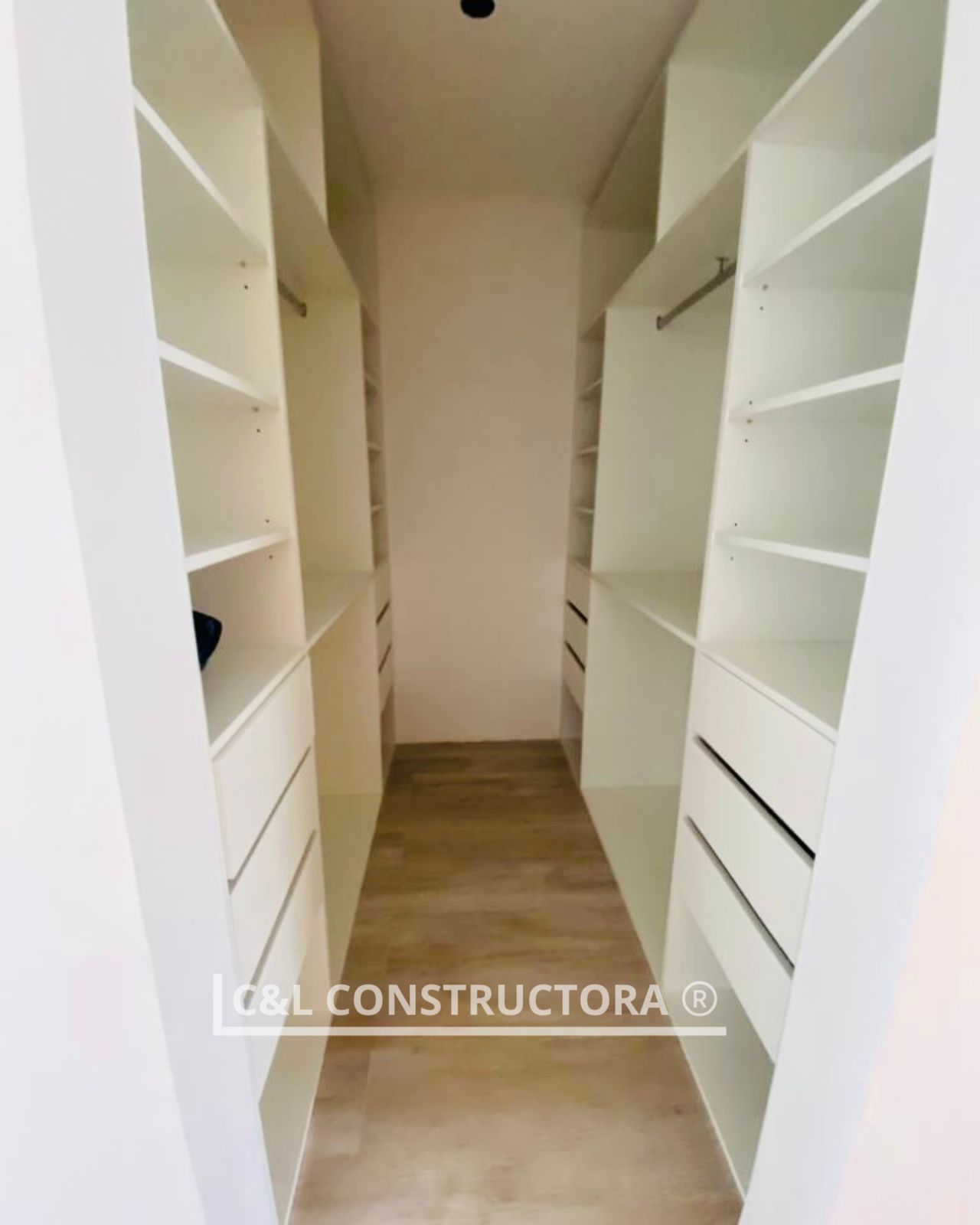 Un vestidor con estantes y cajones blancos a ambos lados, piso beige.
