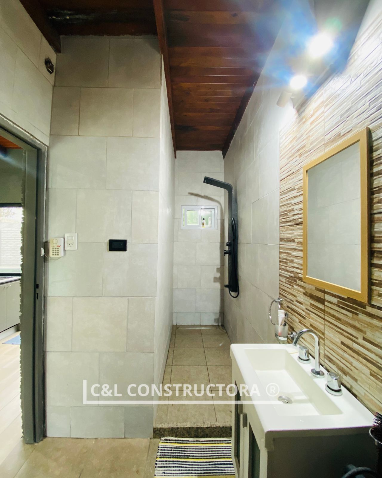 Baño con ducha, lavabo y pared texturizada, azulejos blancos y techo de madera.
