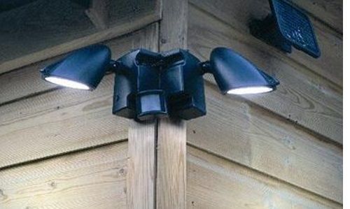 A black security light with a motion sensor attached to a wooden wall.