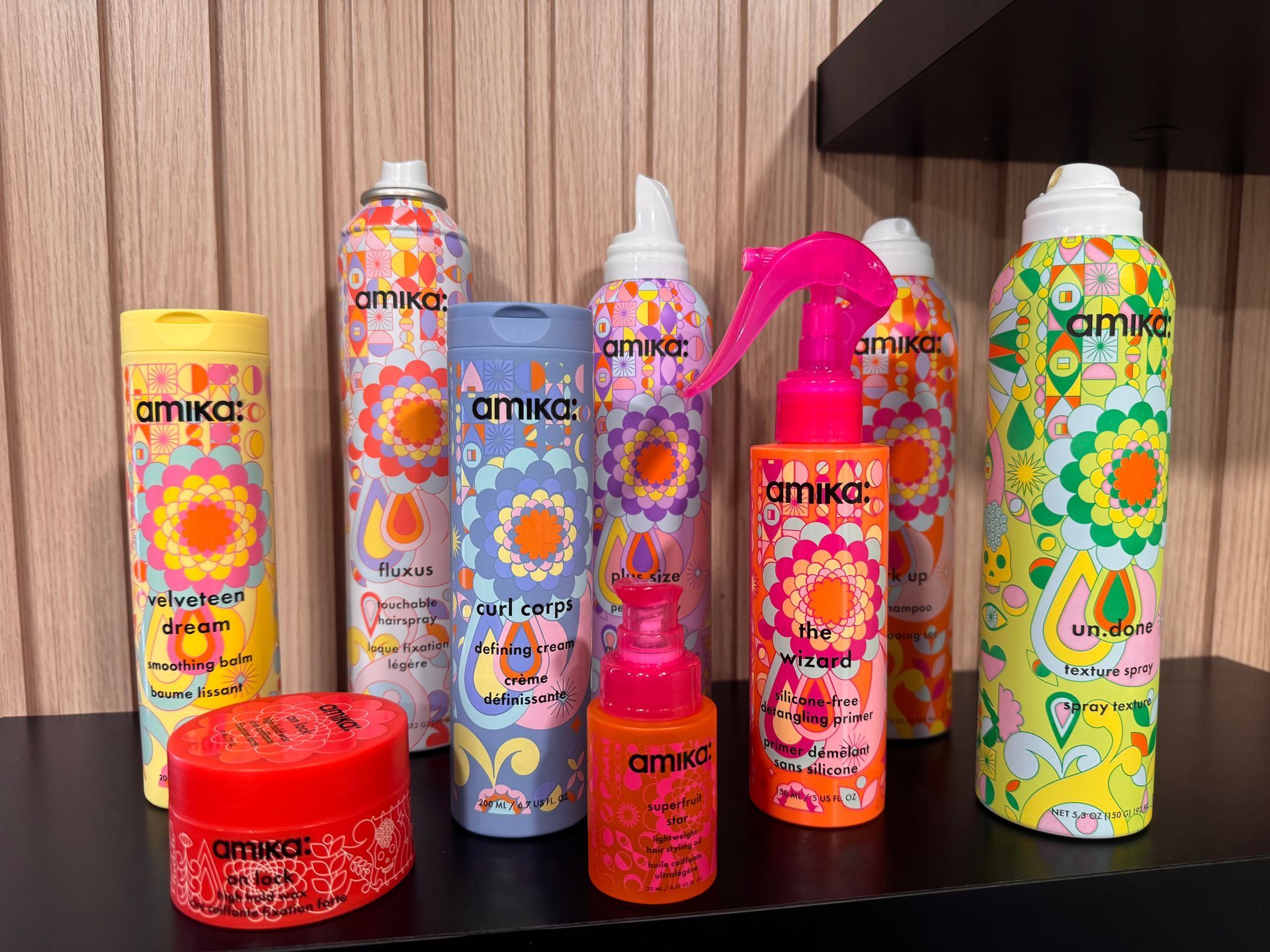Assorted colorful hair care products arranged on a wooden shelf against a wood-paneled wall